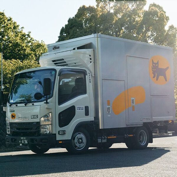 A modern Yamato Transport delivery truck in Japan featuring the Kuroneko black cat logo on the side in a large yellow circle.