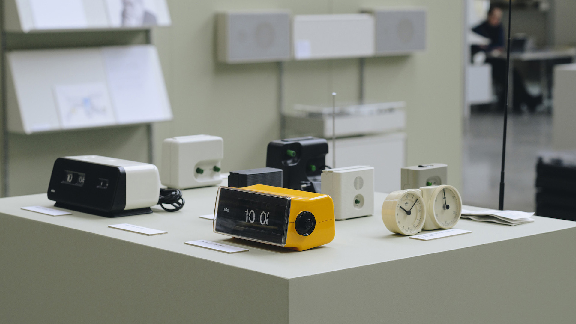 A collection of Braun clocks, radios and other electronic products displayed together, showing a consistent design language across different objects.