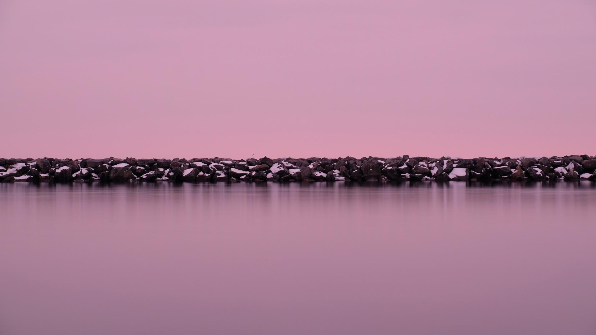 Lake Ontario at dusk, with a snow-covered breakwater beneath a pink sky.